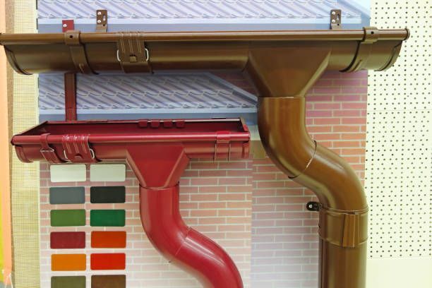 Two metal gutter systems in red and brown, mounted on a brick and paneled background, with a color swatch.