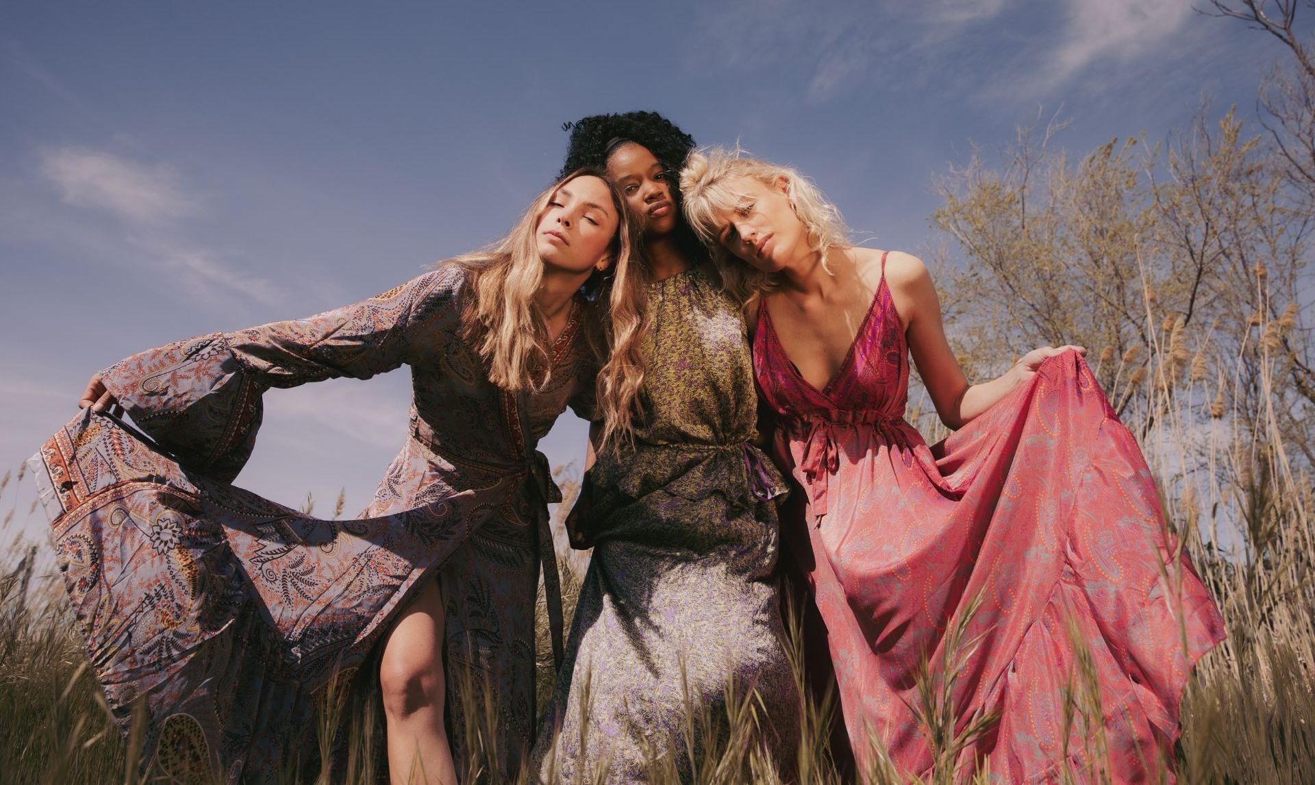Three women in long dresses are standing next to each other in a field.