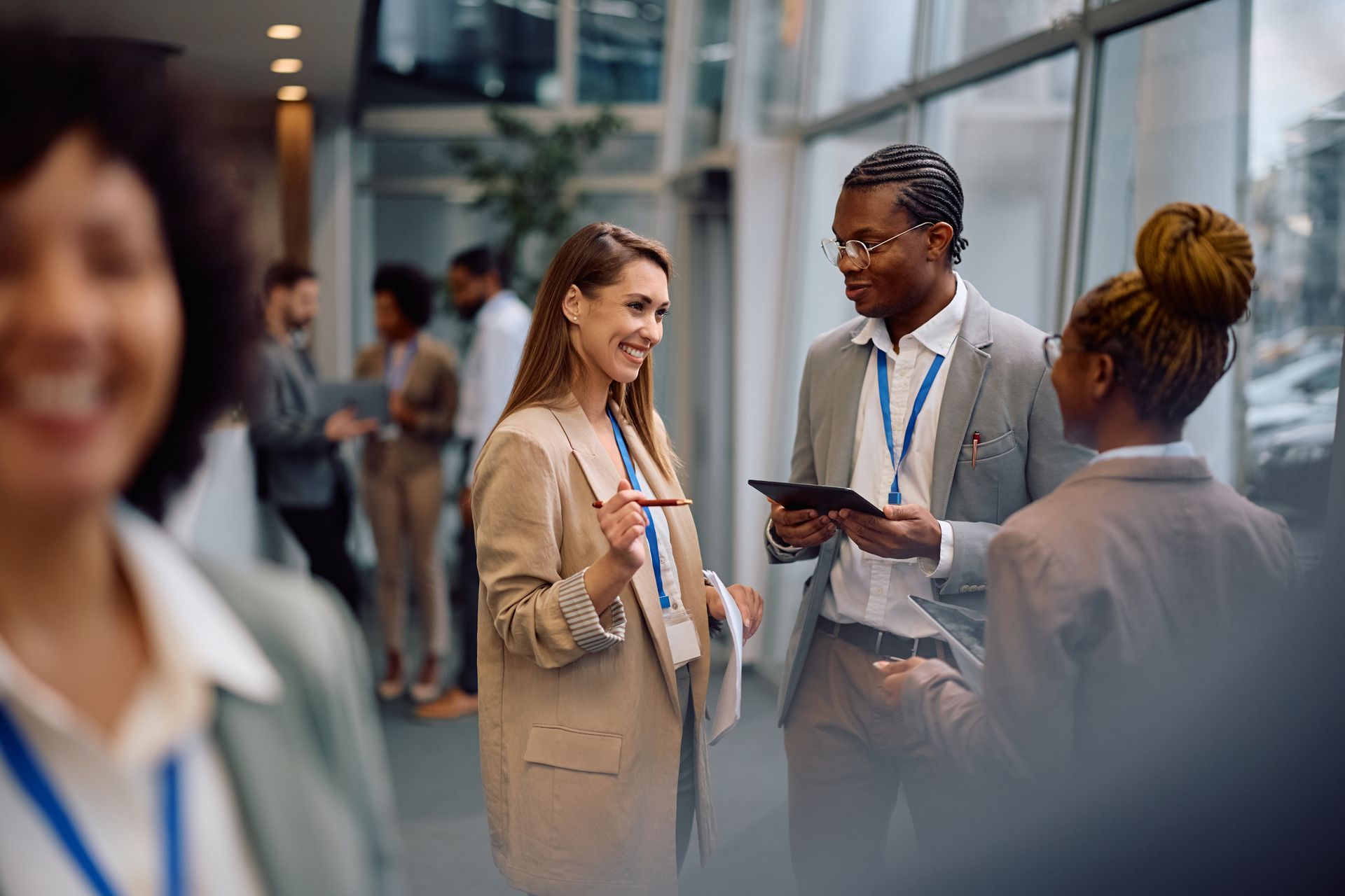 People networking in a well-lit hallway, wearing lanyards and business attire. One person is smiling.