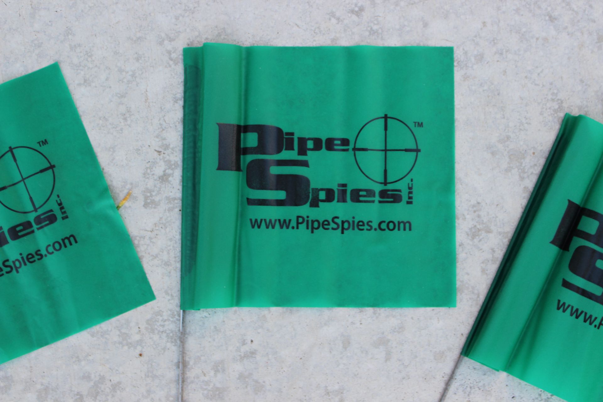 Green Pipe Spies flags on a gray surface. The logo features black text and a crosshair.
