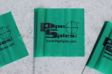 Green Pipe Spies flags on a gray surface. The logo features black text and a crosshair.