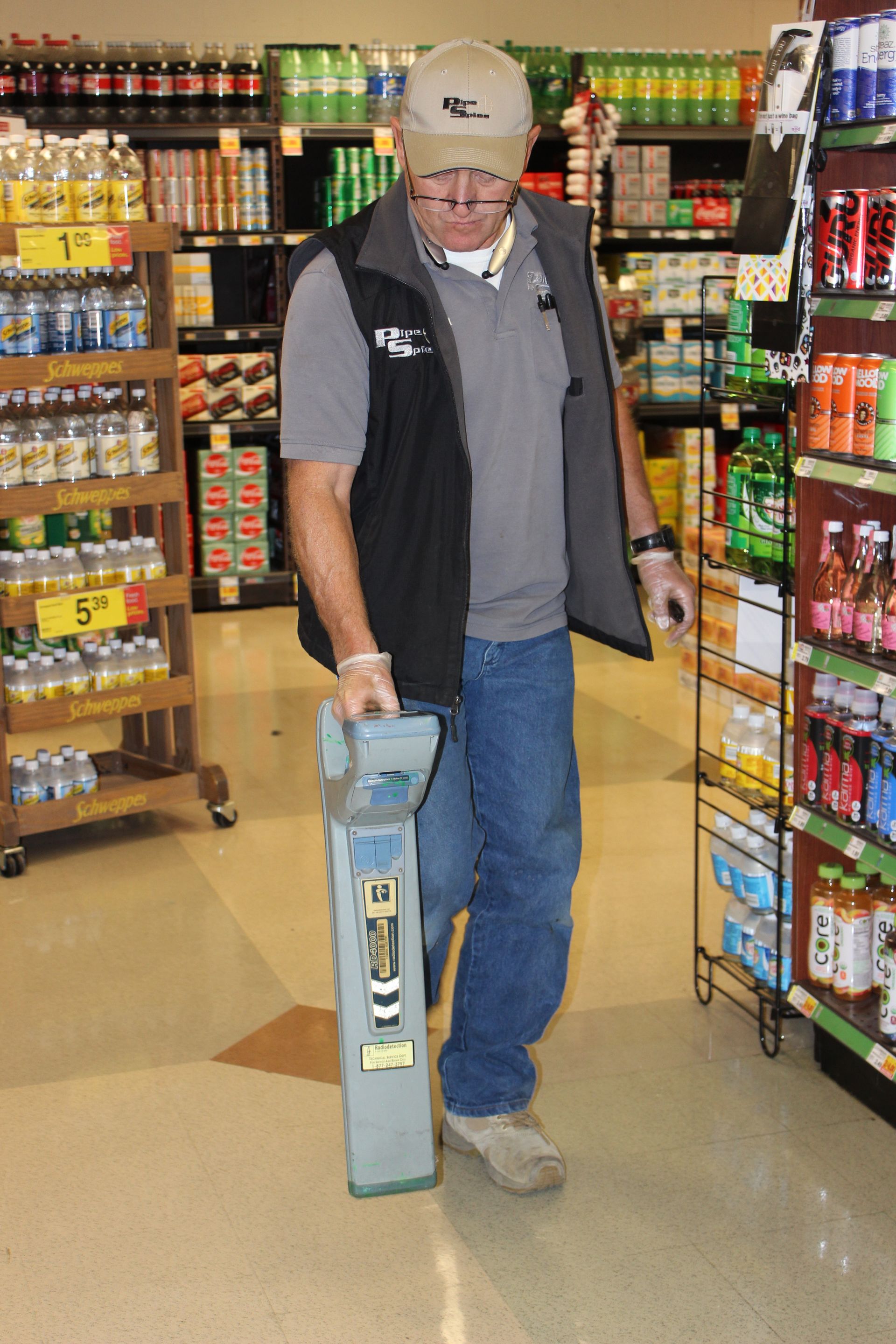 Man in store using a metal detector on the floor between shelves filled with products.