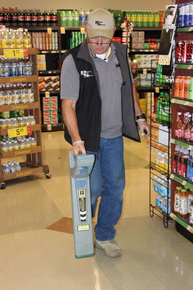 Man in store using a metal detector on the floor between shelves filled with products.