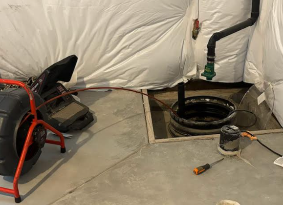 A plumbing inspection setup in a basement: camera near a sump pump, with a screwdriver and other tools present.