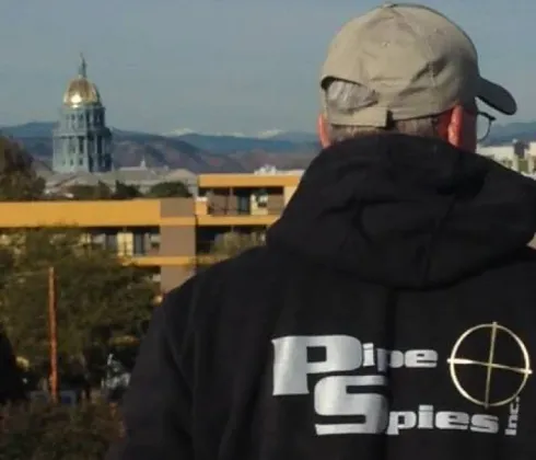 Man in black hoodie with logo, looking at a cityscape with gold-domed building.