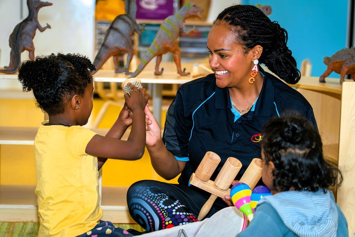 Thornlie Childcare Educator is playing with two little girls in a classroom.