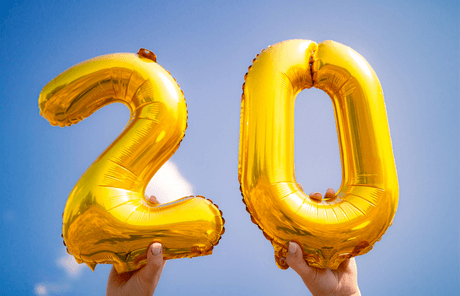 A person is holding a gold balloon in the shape of the number 20.