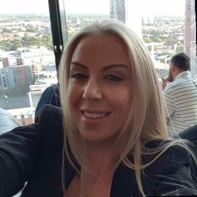 A woman is taking a selfie in front of a window with a city in the background.