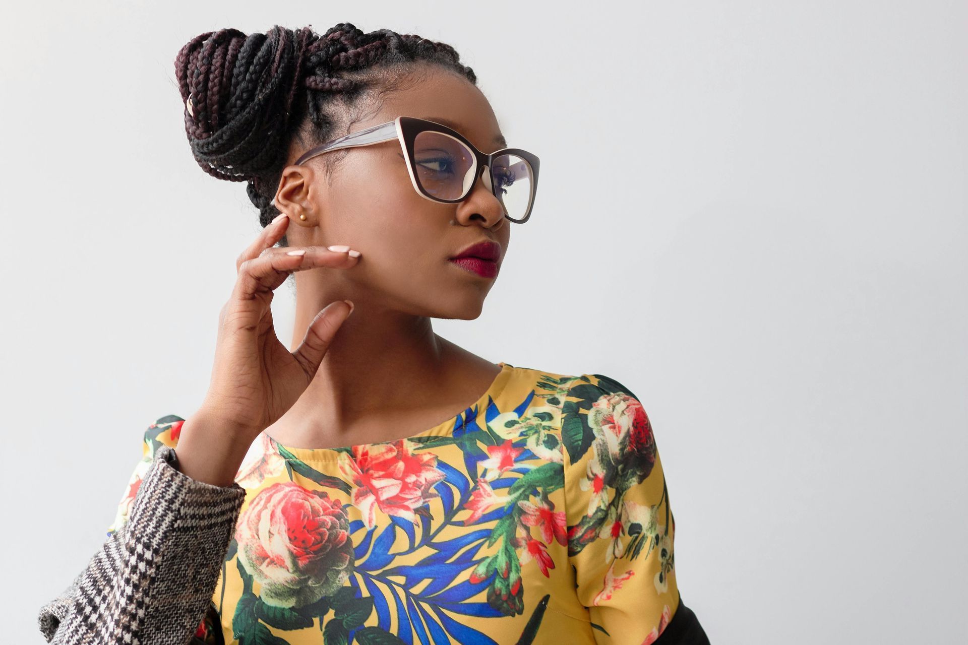 Woman with braided hair, wearing glasses and a floral top, looking to the side.