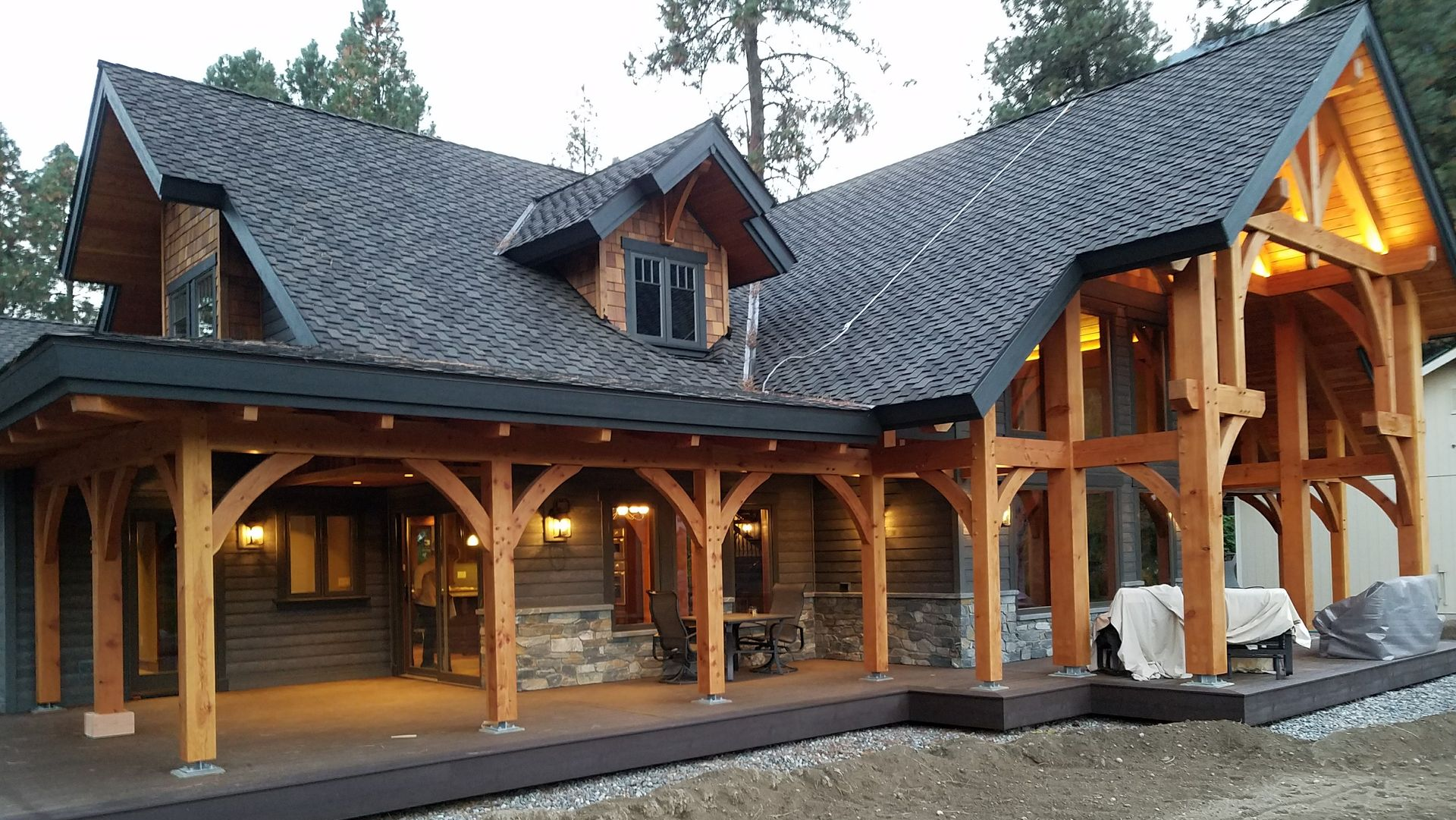 Wooden timber-framed house with porch, dark roof, stone and wooden siding, nestled among trees.