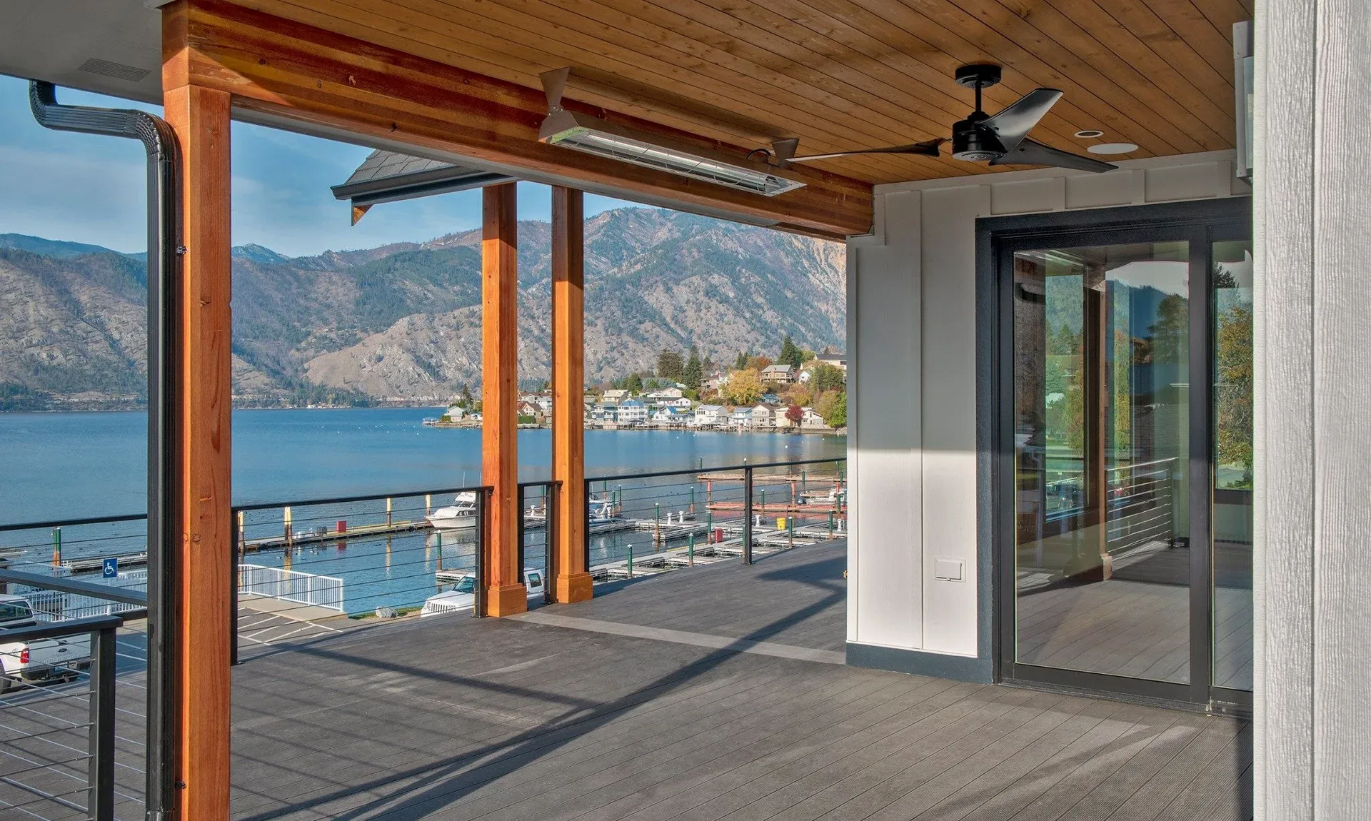 Wooden patio overlooking a lake and mountains. Features a fan, heater, and glass doors.