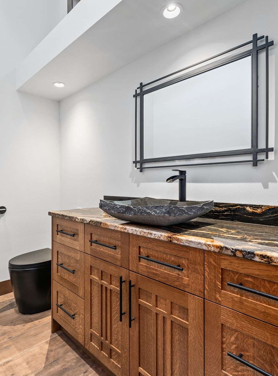 Bathroom with wood vanity, black vessel sink, and framed mirror.