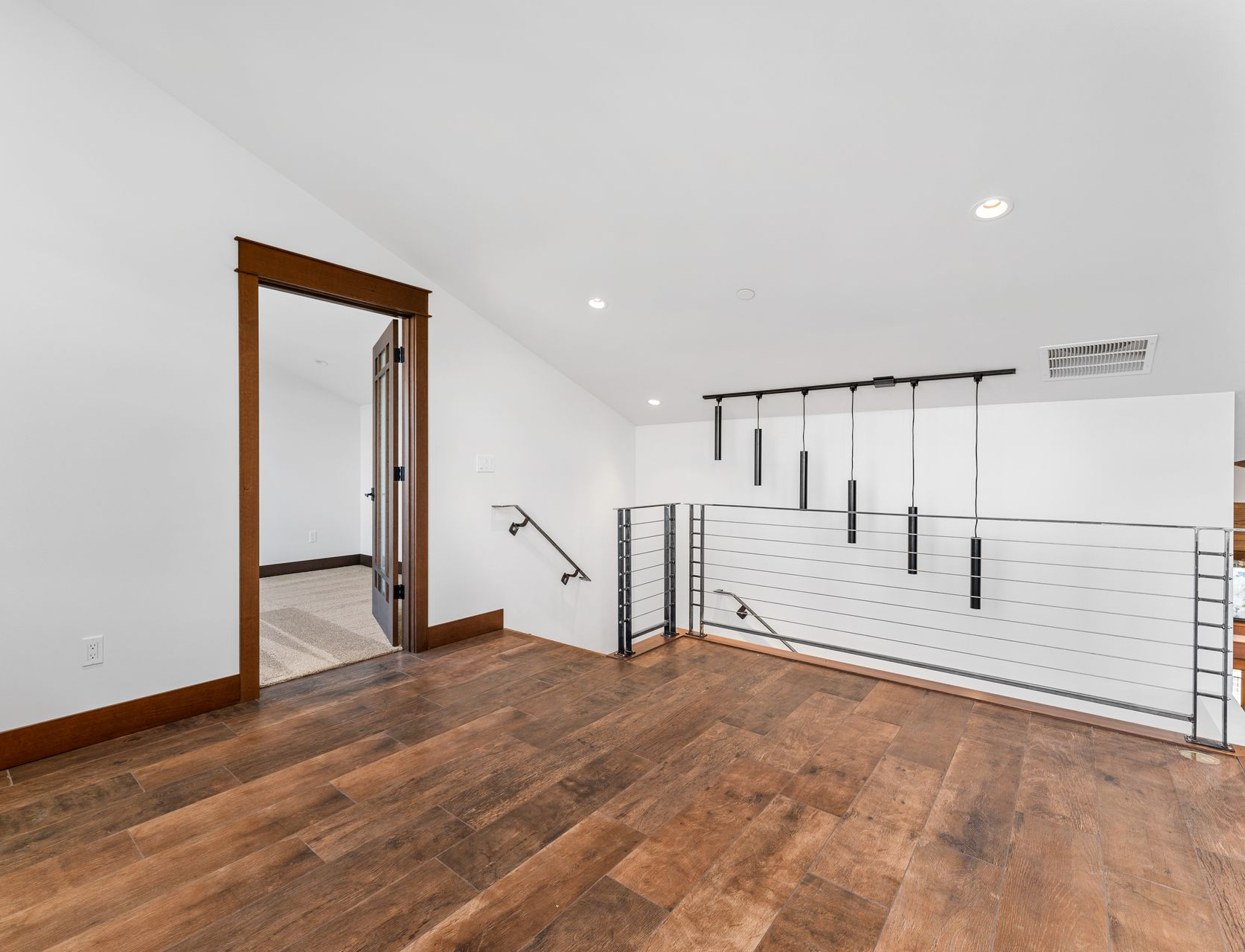Hallway with wood floor and white walls, brown door frame, and modern railing.