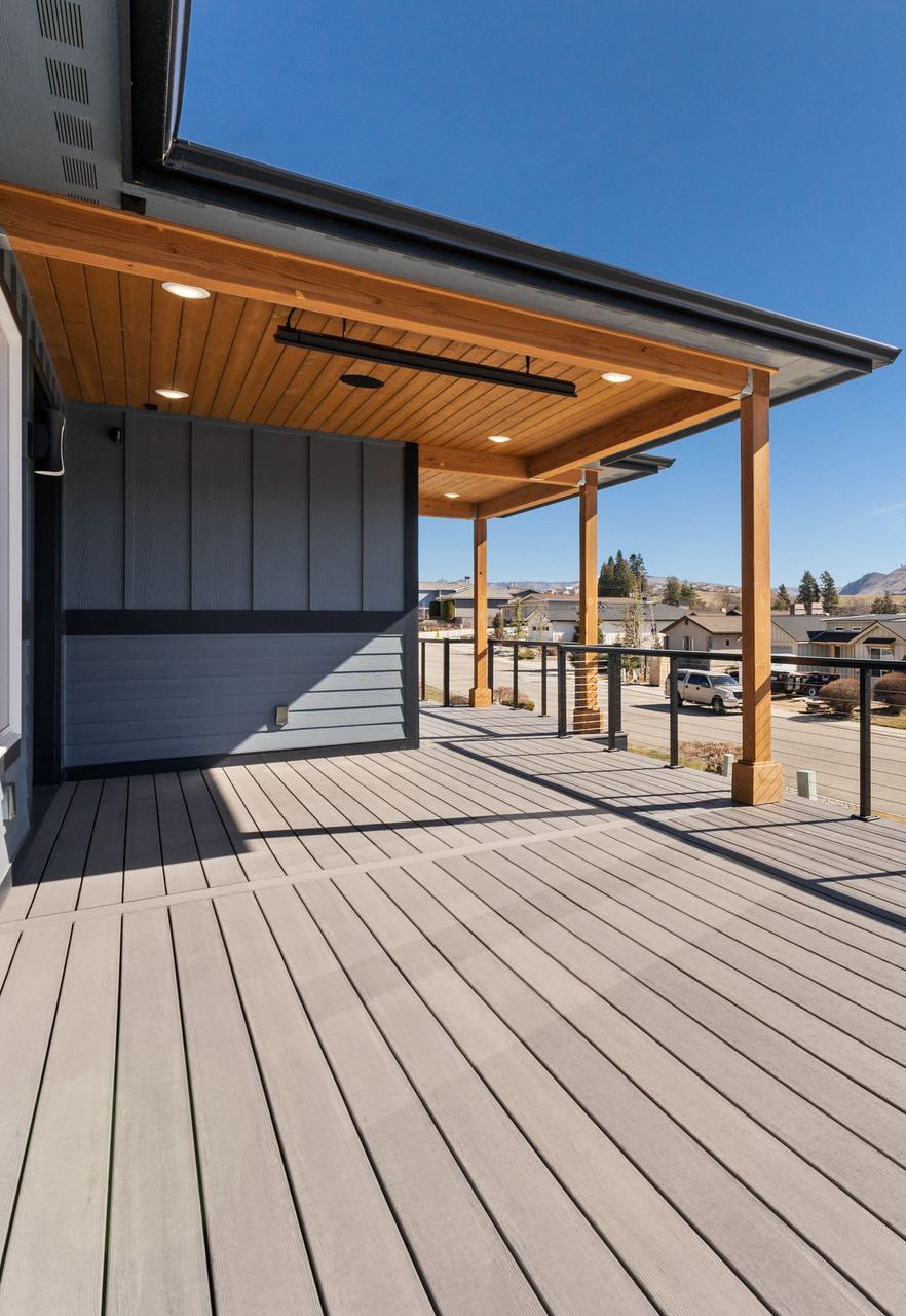 Wooden deck with gray planks and a covered porch with wooden beams and lights; sunny outdoor setting.