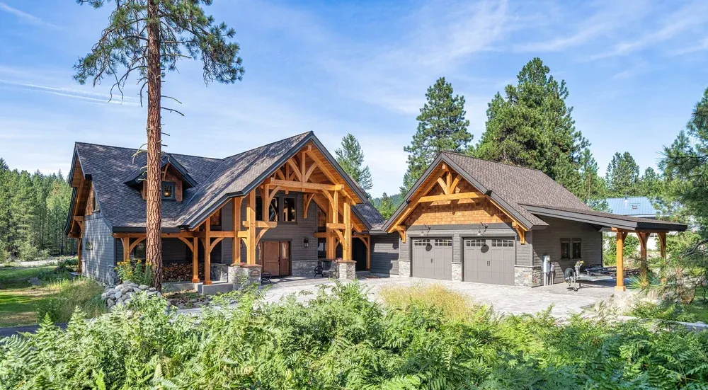 Rustic home with timber frame entrance and attached garage, set in a wooded area on a sunny day.