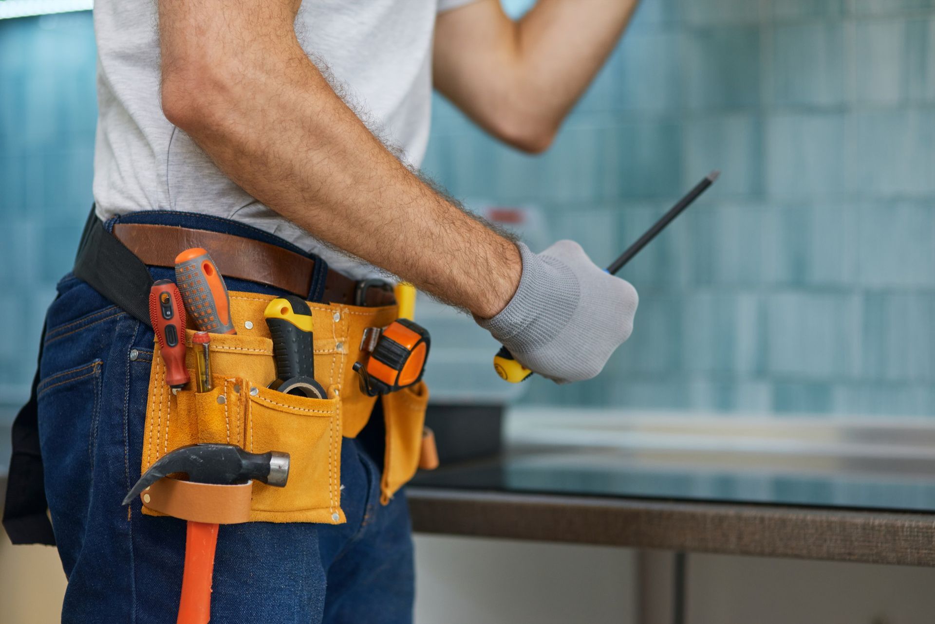 A man is wearing a tool belt and holding a screwdriver.