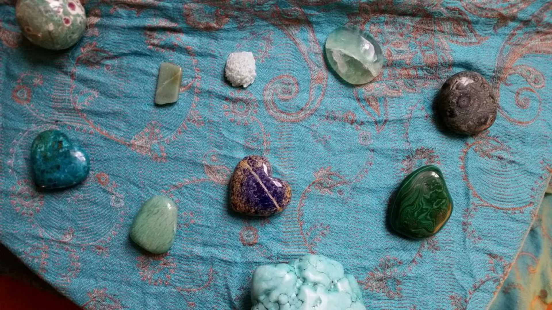 Différentes pierres lisses et colorées disposées sur un tissu bleu sarcelle.