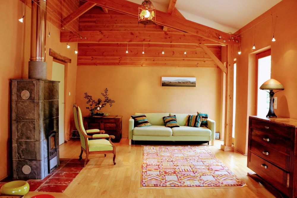 Salon confortable avec poutres en bois, canapé vert clair, tapis coloré et cheminée en pierre.