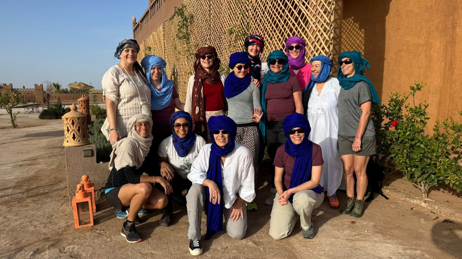 Groupe de personnes portant des foulards, posant à l'extérieur près d'un bâtiment rustique.