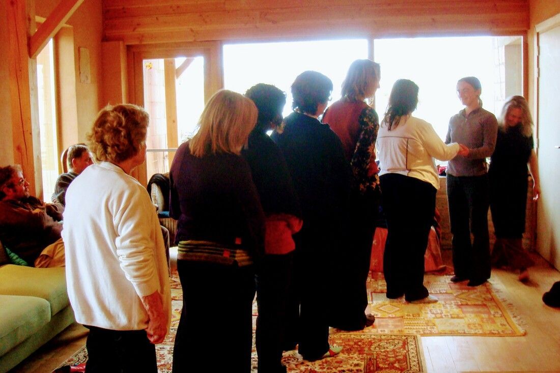 Groupe de personnes à l'intérieur d'une pièce lumineuse ; certaines debout, quelques-unes près d'une fenêtre, d'autres assises sur un canapé.