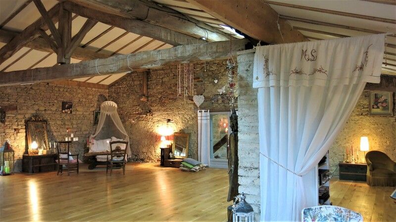 Chambre avec parquet, murs en pierre, poutres apparentes et un coin lit drapé, éclairé par des lampes chaleureuses.