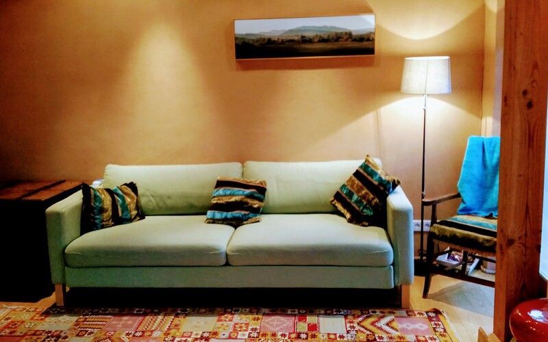 Un salon confortable avec un canapé vert, des coussins à motifs, un lampadaire et une chaise en bois.