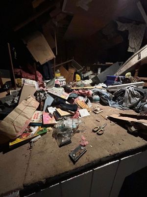 A cluttered attic space with scattered boxes, personal items, and debris under dim lighting.