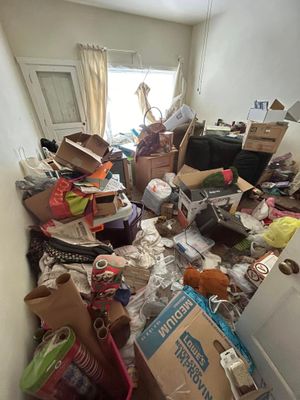 A small room cluttered with cardboard boxes, bags, and miscellaneous household items scattered across the floor.