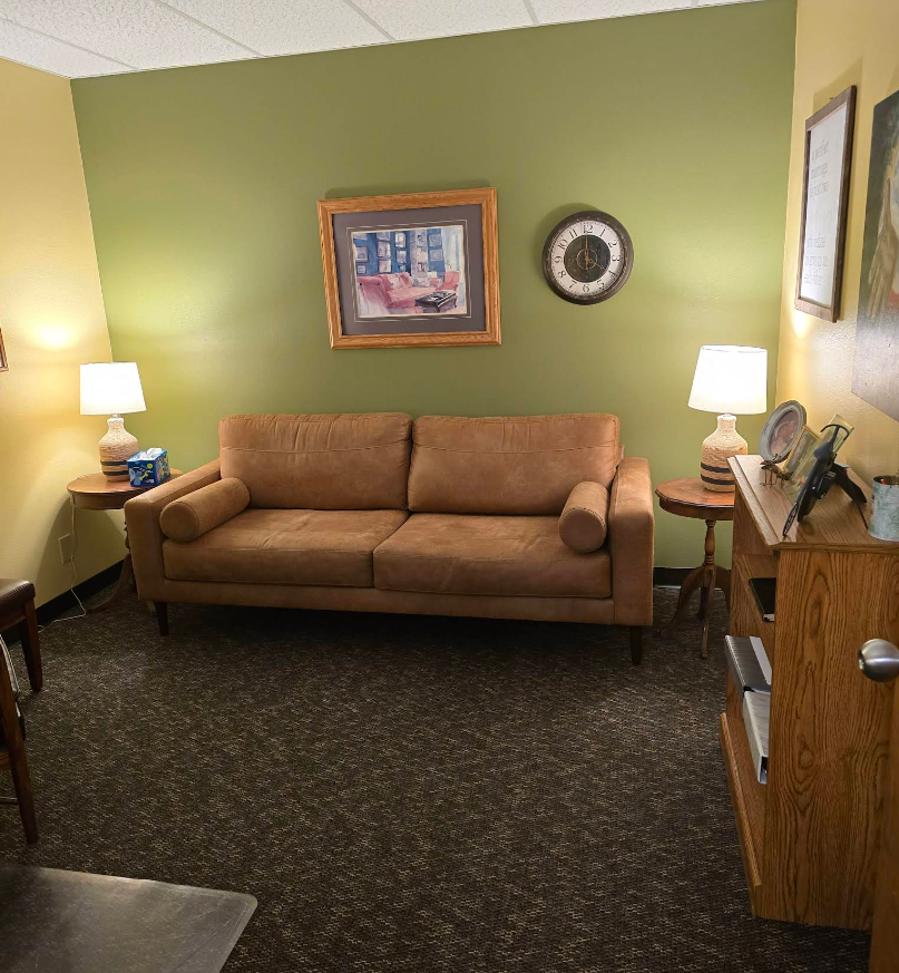 Couple on a sofa in therapy session; counselor in foreground, abstract art on wall.