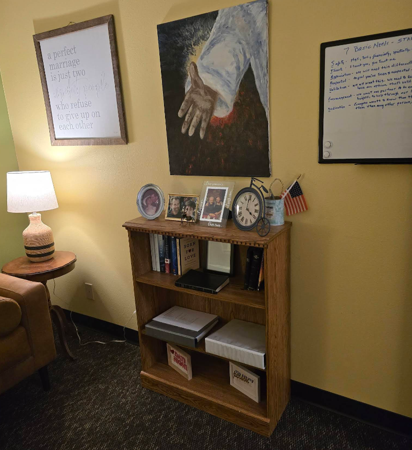 Woman and man in chairs, light-filled room; woman reads, man smiles looking at camera.
