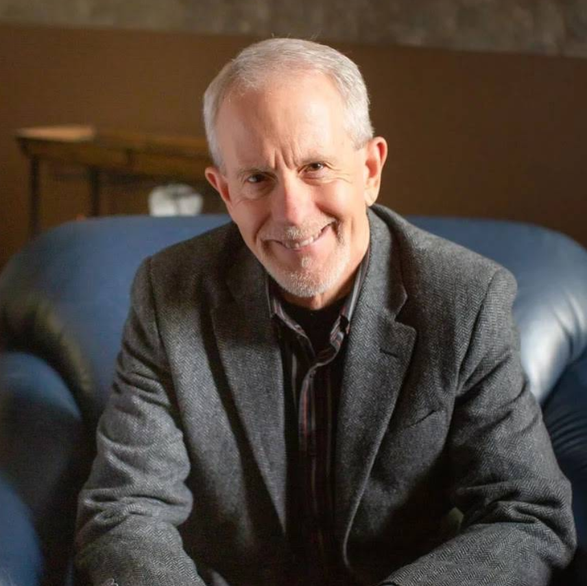Woman taking notes as man gestures while seated in a counseling session.