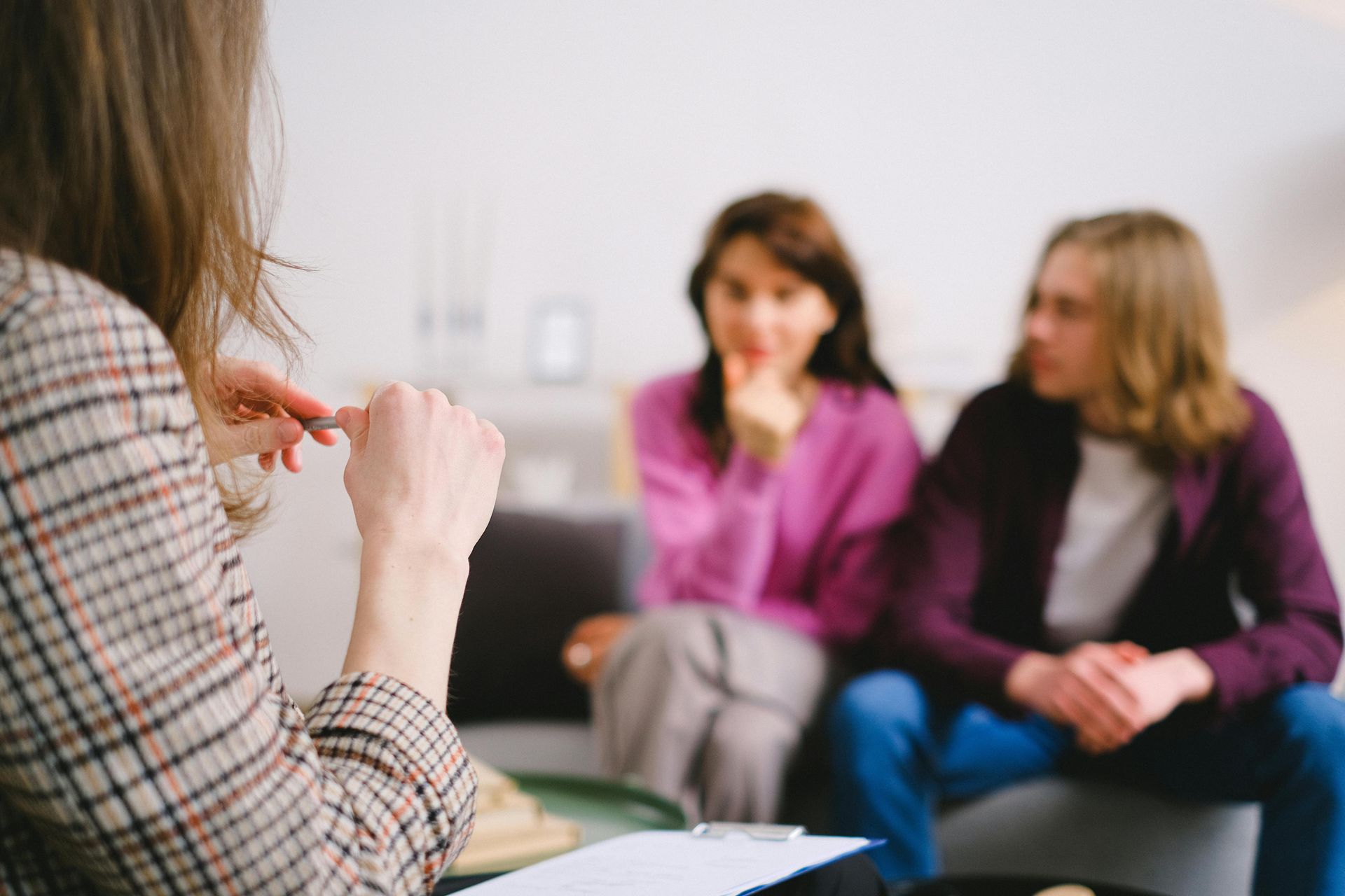 A therapist in a plaid jacket consults with a couple sitting on a couch.