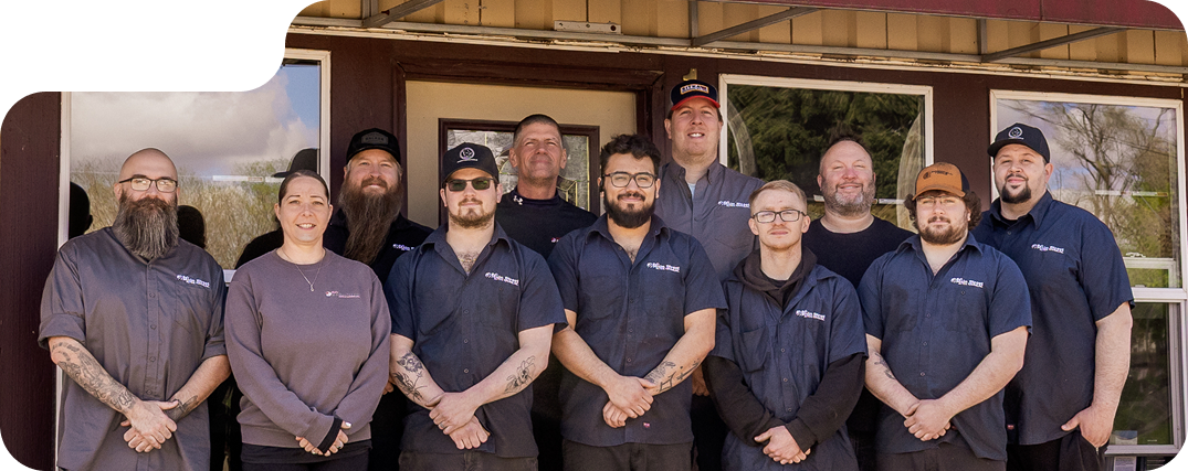 Group of eleven people in navy shirts standing outside a storefront, smiling at the camera. | Bob's Main Street Auto & Towing