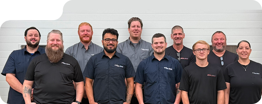 Group of nine people standing together indoors, smiling in front of a light gray wall | Bob's Main Street Auto & Towing