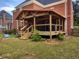 A wooden porch is being built in the backyard of a brick house.