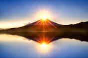 The sun is reflected in the water of a lake with a mountain in the background.