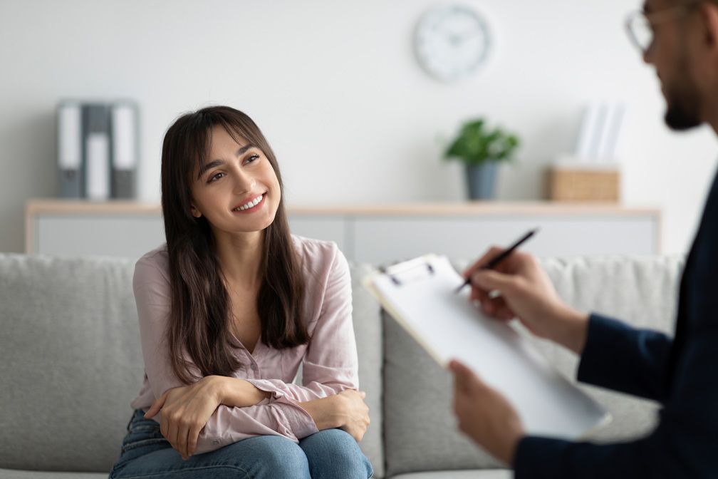 A woman is sitting on a couch talking to a doctor.