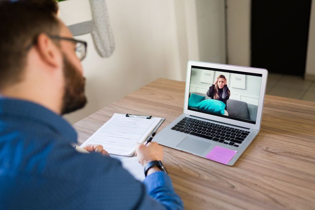 A woman is sitting on a couch talking to a doctor.