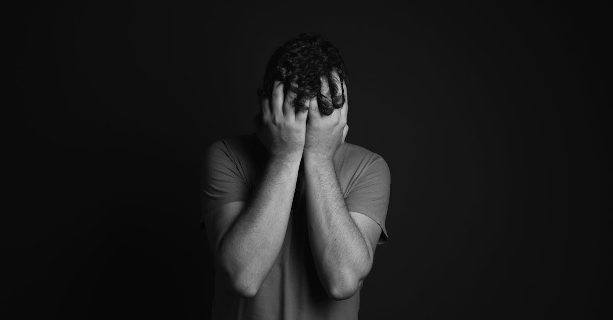 A man is covering his face with his hands in a black and white photo.