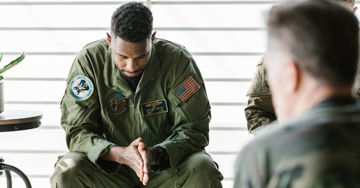 A man in a military uniform is sitting down with his hands folded in prayer.