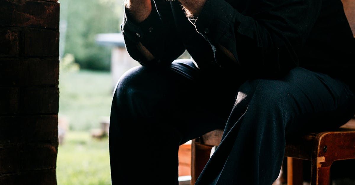 A man is sitting on a wooden stool with his legs crossed.