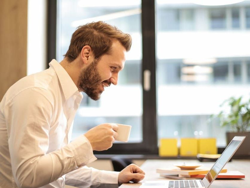 A man is drinking coffee while using a laptop computer.