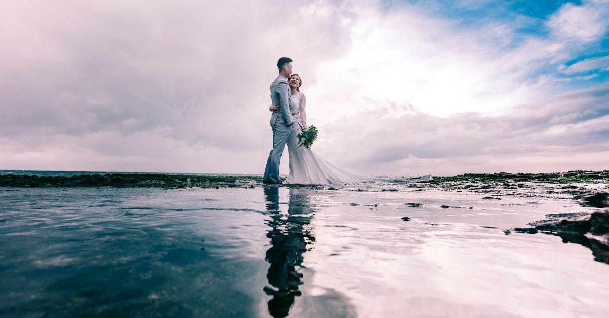 A bride and groom are standing in the water on the beach.