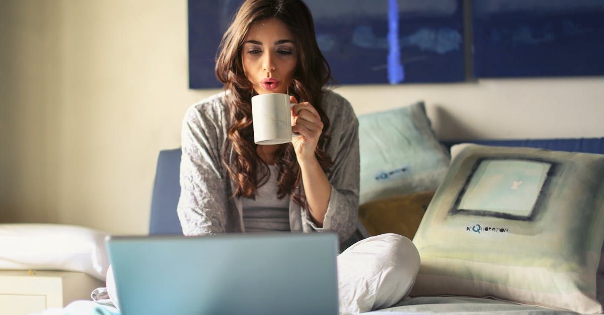 A man is drinking coffee while using a laptop computer.