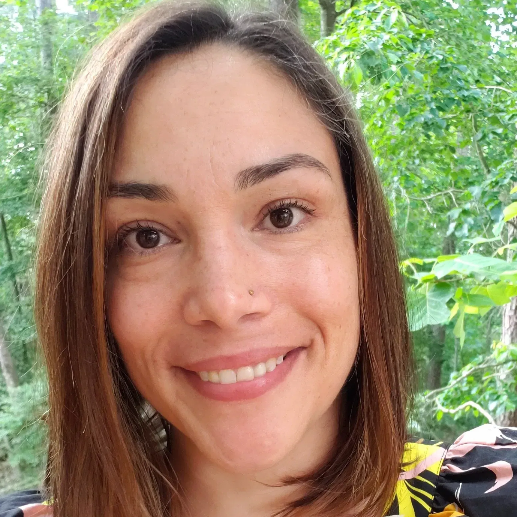 A close up of a woman 's face smiling in front of trees.