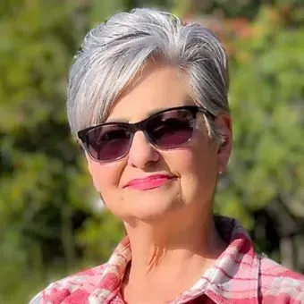 A woman with gray hair is wearing sunglasses and a plaid shirt.