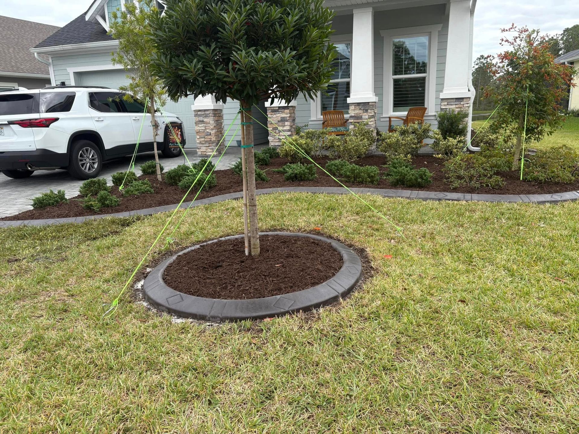 A white suv is parked in front of a house with a tree in the middle of the yard.