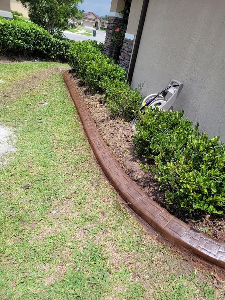 A concrete curb is surrounded by bushes and grass in front of a house.