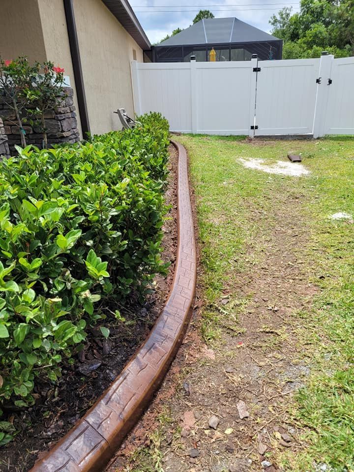 A concrete curb in a yard next to a white fence.