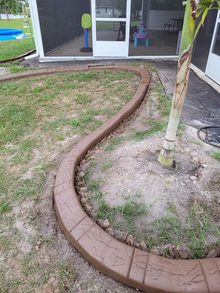 A concrete curb is surrounding a tree in a backyard.